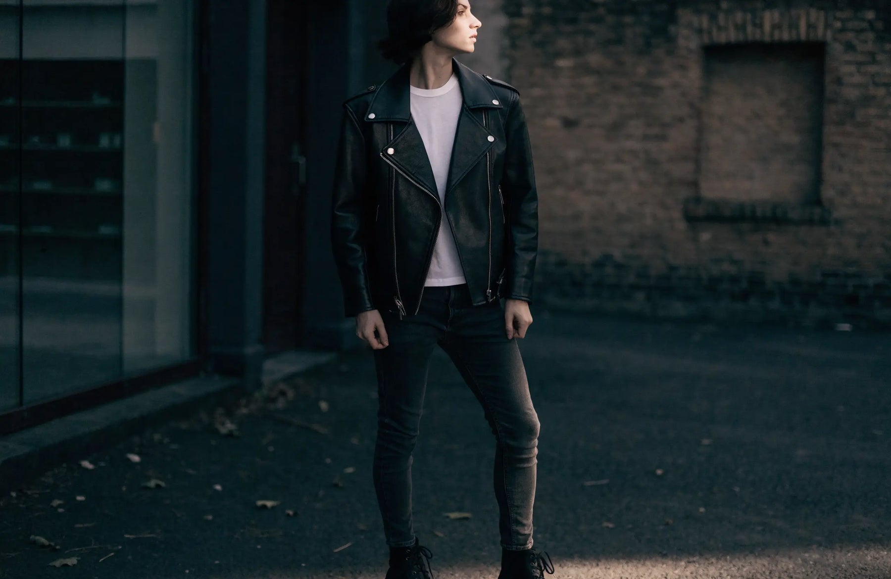 Person wearing a black leather biker jacket with an asymmetric zipper, white t-shirt and jeans