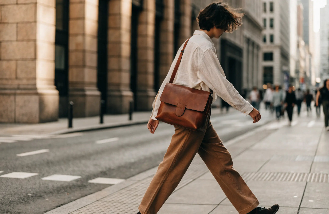 Brown leather messenger bag worn cross-body over a casual outfit while commuting
