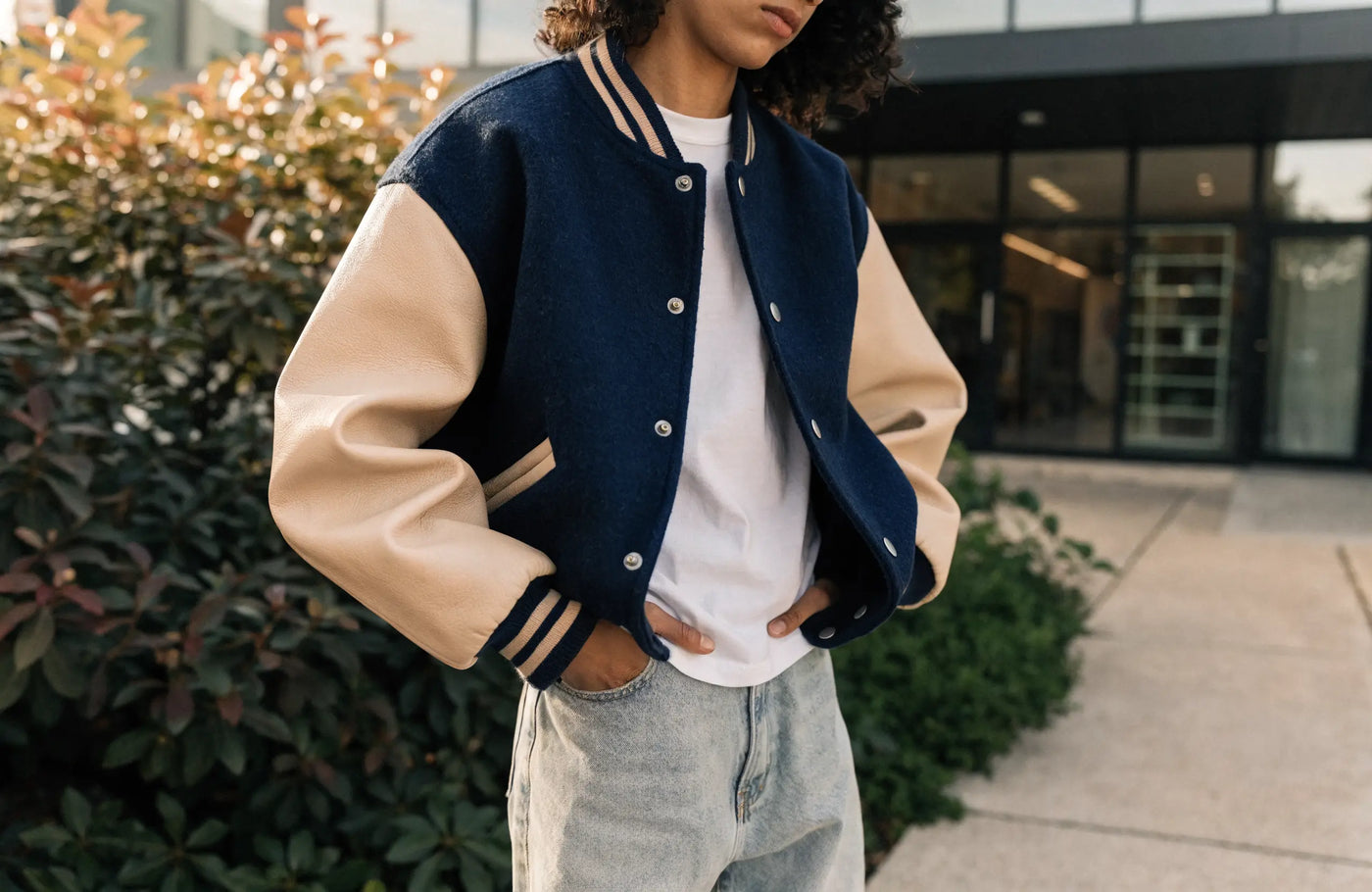 Person wearing a navy and cream varsity letterman jacket with leather sleeves and jeans
